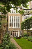 Circular metal sculpture on lawn in front of courtyard facade of three-storey house with white lattice windows