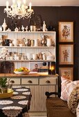 Country-house-style dining area with white dresser crammed with collection of jugs, ornaments and china bowls against dark brown wall