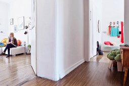 Hallway with open doors; woman sitting in living room and coat rack on wall above pouffe