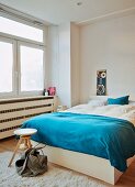 Blaue Tagesdecke auf französischem Bett, an Bettende Drehhocker aus Holz in minimalistischem Schlafzimmer