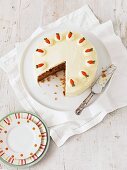 Carrot cake on a cake plate with a large slice cut out of it