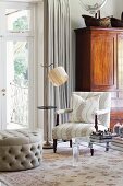 Armchair and cushion covered in matching fabric next to standard lamp and antique cupboard in background