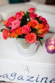 Vase mit Rosenstrauss und Windlicht auf beschriftetem Truhentisch