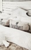 Detail of bed with bolsters, pillows and carved wooden headboard painted white