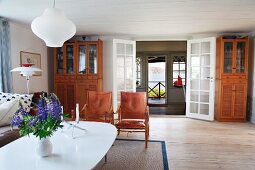 Vase of flowers on white, oval table and classic armchair in spacious living area in Swedish wooden house
