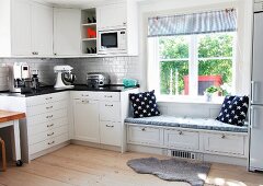 Corner unit in Swedish, country-house kitchen with blue and white accessories on integrated window seat