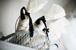 weiße Tüten mit schwarzem Schleifenband im Drahtkorb