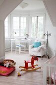 Kinderzimmer mit Schaukelpferd und Spielzeugkiste auf Dielenboden, im Hintergrund Sessel und Tisch vor Fenster im Erkerbereich
