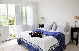 Doppelbett mit blau-weiss gemusterter Tagesdecke, seitlich Nachtkästchen aus dunklem Holz im Schlafzimmer