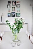Bouquet in glass vase and tealight holders on white dining table