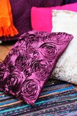 Cushion with silk-effect, purple cover and pattern of roses on rag rug