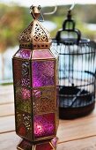 Bronze-coloured, Oriental-style metal lantern with coloured glass panels on wooden terrace