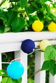 String of colourful spherical lanterns draped on white balustrade and green leaves in garden