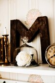 White, fabric rose under glass cover and ornamental letter on white shelf