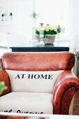 Heller Stoffbezug mit Aufschrift 'AT HOME' auf Rücken und Sitzfläche eines traditionellen, ledernen Clubsessels