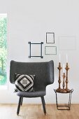 Armchair with scatter cushion next to set of candlesticks on side table below washi tape picture frames on wall