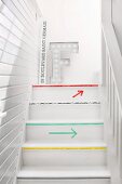 Wooden staircase in narrow stairwell with white, wood-clad walls; treads edged with colourful washi tape and washi tape arrows