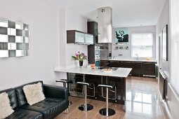 A leather sofa and a fitted kitchen with barstools at a counter; part of a long, open-plan living area with a polished, ceramic-tiled floor