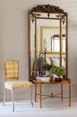 Rococo chair with white and yellow gingham upholstery next to side table below mirror with ornate frame