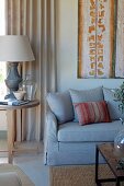 Couch with pale grey upholstery next to table lamp on side table