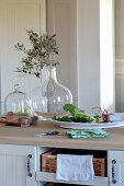 Olive branch in glass vase next to bowl of fresh vegetables on kitchen counter