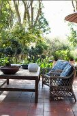 Rattanstühle und Holztisch mit Bonsai auf Terracotta-Terrasse und Garten im Hintergrund