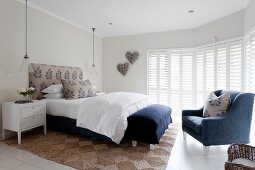 Elegant white bedroom with blue accents, blue armchair and blue bench at foot of bed