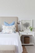 Double bed with white bedspread, arranged scatter cushions and white-painted bedside table