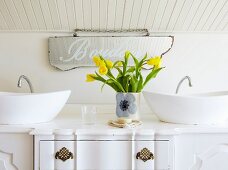 Vintage chest of drawers converted into washstand with twin countertop basins; vase of yellow tulips