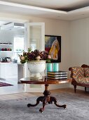 Large pot of proteas on antique, round table in front of open double doors with view into kitchen