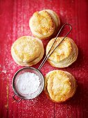 Mince pies and a sieve of icing sugar on a red wooden surface