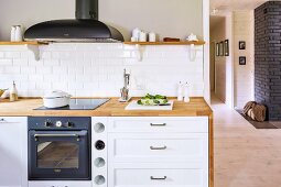 Kitchen counter with wooden worksurface and built-in cooker below extractor hood next to cabinet with white drawer fronts