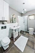 White and grey bathroom - washstand with white, turned legs against half-height tiling on wall and floor-level glass shower cubicle