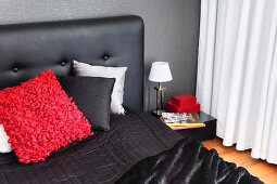 Scatter cushions on black bed with upholstered headboard against dark wall