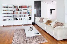Long, pale sofa with fur scatter cushions, coffee table on flokati-style rug and shelving units with base cabinets against wall