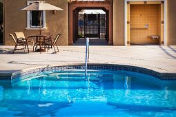 Pool mit Einstieg und Edelstahl Geländer an Treppe, im Hintergrund Sitzplatz mit Sonnenschirm vor Wohnhaus, seitlich in Hausnische eingebauter, offener Duschraum