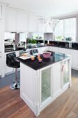 An island counter in an elegant fitted kitchen with a crystal pendant light and lilac coloured baking moulds on a reflective work surface
