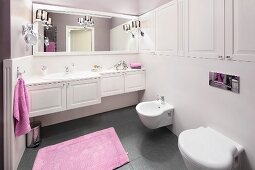 Lilac towels giving a touch of colour to an elegant bathroom with white, built-in cupboards and a grey floor