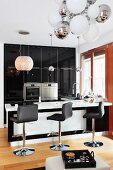 Schwarzweisse Designerküche mit hochglänzenden Fronten, Lederhocker an Frühstücksbar und verschiedenen Kugelleuchten