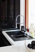 An anthracite coloured sink with a pull-down sprayer mixer tap set into a white work surface with a shiny black cupboard in the background