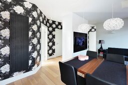 A view from a dining area with a wooden table laid with black table runners towards a hallway with black and white floral wallpaper