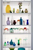 Glasses and vases of various colours and styles on modern shelves