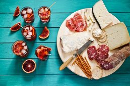 An Italian appetiser platter next to glasses of aperitifs garnished with slices of blood orange