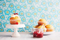 A muffin topped with cream, redcurrants and redcurrant compote against a floral papered wall