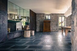 Sparsely furnished interior with charcoal stone floor in converted Italian farmhouse; stone walls contrasting with mirrored cupboards
