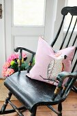 Nostalgischer Holzschaukelstuhl mit rosafarbenem Dekokissen in nordischem Landhausambiente