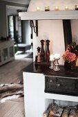 Lit candles on hob of wood-burning oven with firewood and chimney in open-plan living area of country house