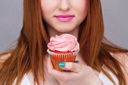 A young woman holding a pink cupcake, face cropped