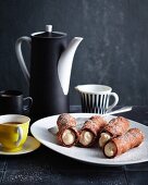 Dark ricotta cannoli on a plate with a jug of coffee