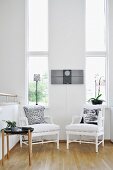 weiße Sessel und Beistelltisch vor Wand mit schmalen, hohen Fenstern
